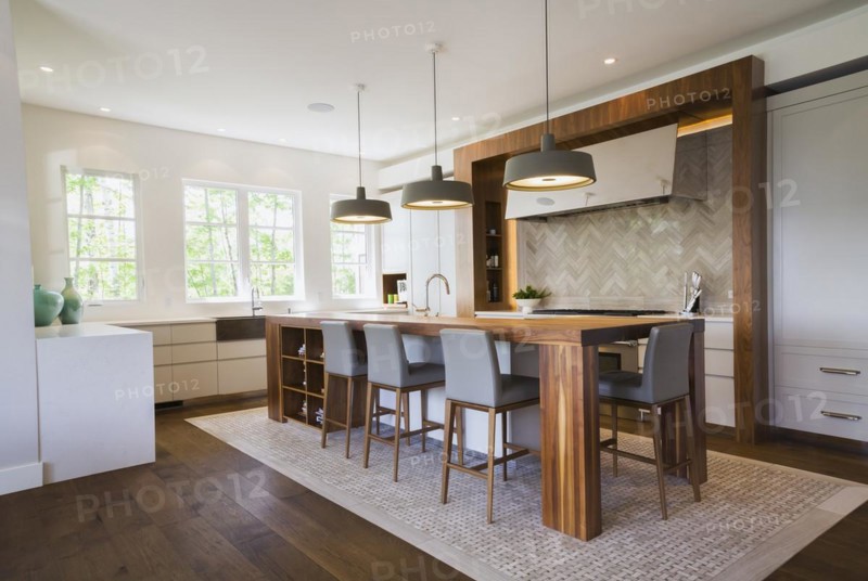 Walnut wood island with grey leather and wooden high chairs on travertine mosaic floor surrounded by engineered hickory wood floorboards in kitchen inside a luxurious contemporary bungalow style home, Quebec, Canada, North America
