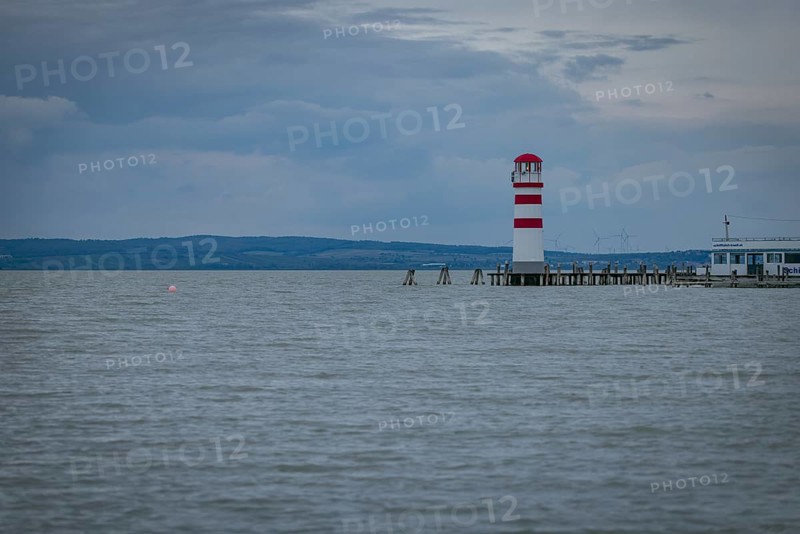 Red and white lighthouse stands on a calm lake under a cloudy sky, Podersdorf, Burgenland, Austria, Europe