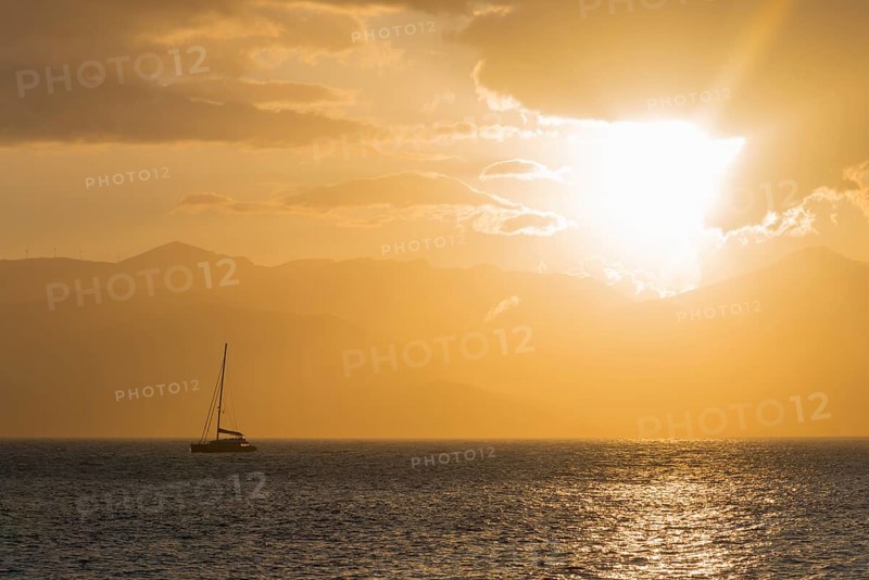 A sailboat on a calm sea at sunset with a golden sky and mountains in the background, Agia Kyriaki, Nafplio, Nauplia, Nauplion, Nafplion, Argolis, Argolic Gulf, Peloponnese