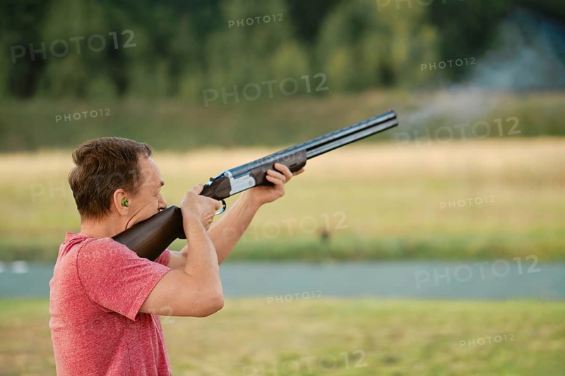An old man shoots from a hunting rifle at a shooting range. Smoke from the barrel is visible in the frame