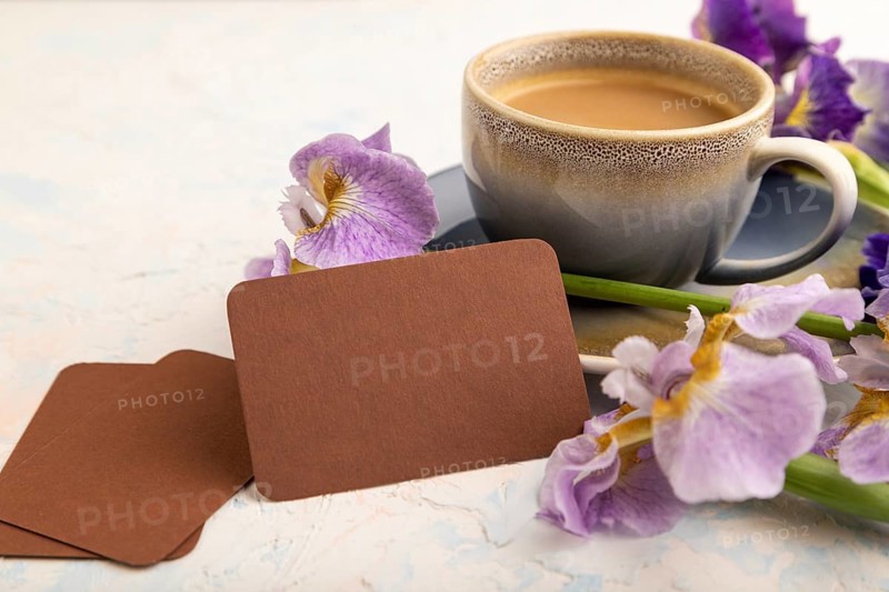 Brown business card with cup of cioffee and iris flowers on white concrete background. side view, copy space, still life. Breakfast, morning, spring concept