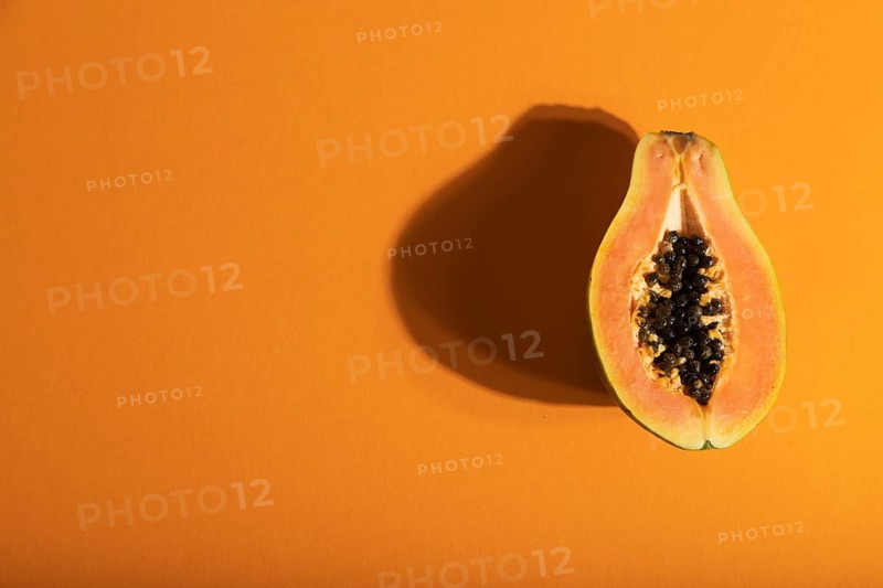 Ripe cut papaya on orange pastel background. Top view, flat lay, copy space, hard light. Tropical, healthy food, women health concept, minimalism