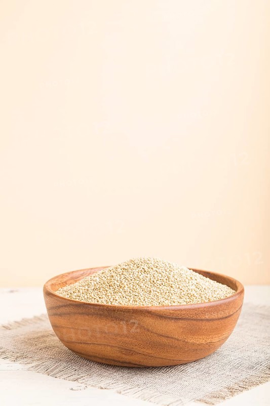 Wooden bowl with raw white quinoa seeds on a white and orange background and linen textile. Side view, close up, selective focus