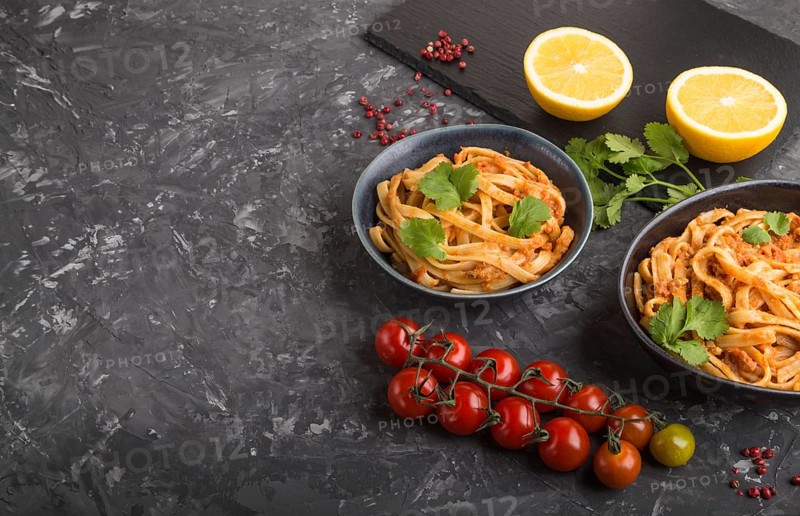 Semolina pasta with tomato pesto sauce, orange and herbs in bowls on a black concrete background. Side view, copy space