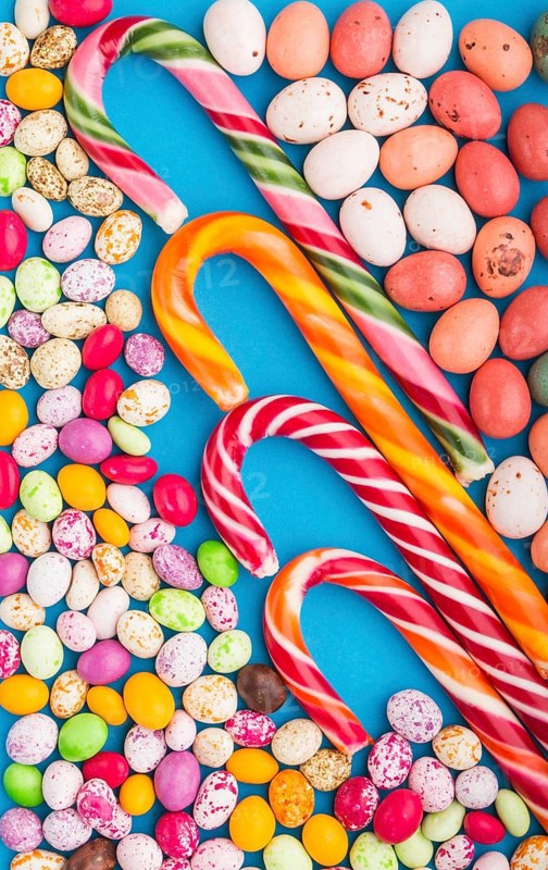 Colorful multicolored candies on a blue background. Christmas cane, chocolate eggs, caramel dragees. top view, flat lay, close up