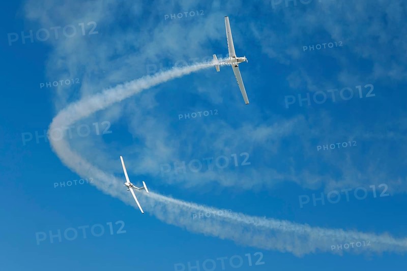 Stunt aerobatic plane performing stunts in blue sky with smoke trail. Concept of teamwork, collaboration, coordination, trust, precision, difficulty, challenge, speed, synergy