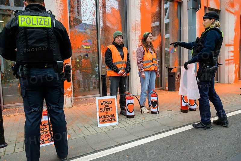 Police officer confiscates Last Generation banner after colour attack on Total Energies building. On a sign: World LNG summit = worldwide catastrophe, Berlin, 06.11.2024