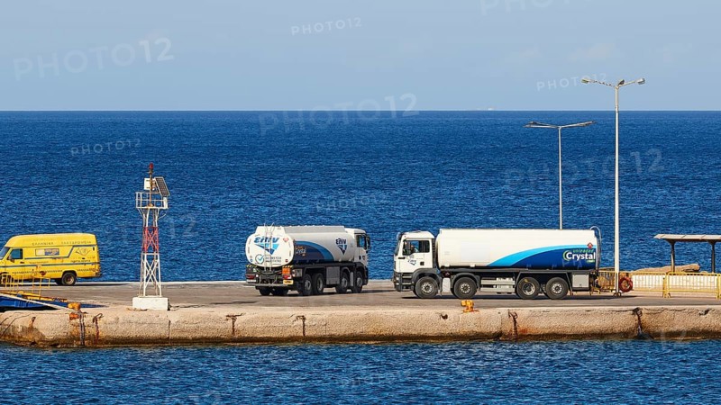 Several lorries standing at the harbour next to the deep blue sea on a clear day, tanker, Pigadia, town and harbour, Pigadia Bay, main town, Karpathos, Dodecanese, Greek Islands, Greece, Europe
