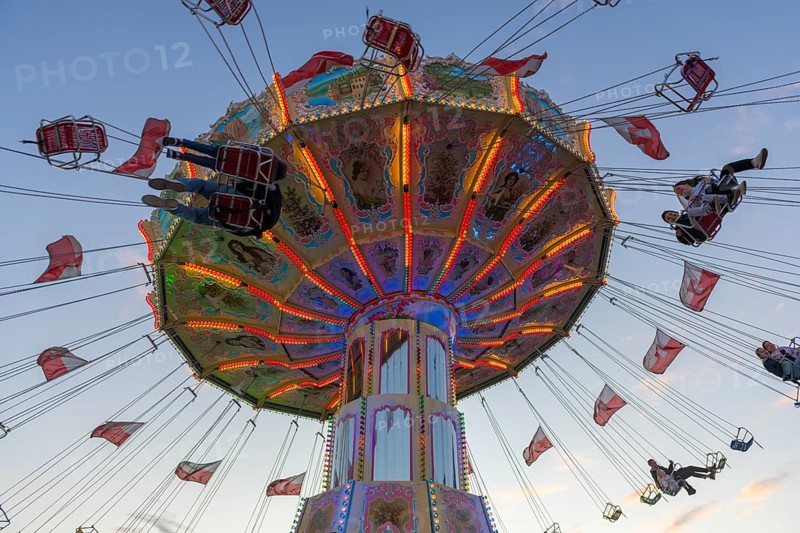 A colourfully illuminated carousel with swinging seats against an evening sky, wave flight, chain carousel, Bad Cannstatt, Stuttgart, Baden-Württemberg, Germany, Europe