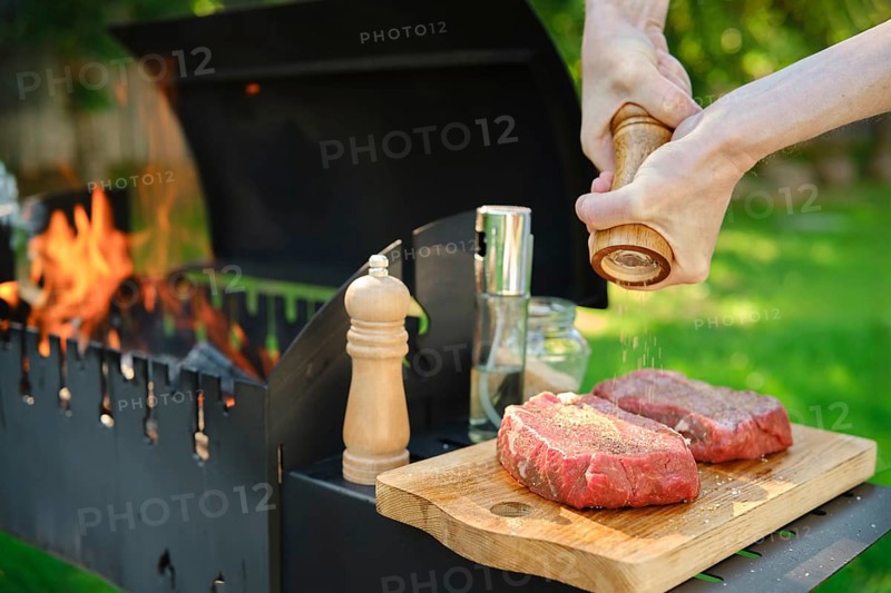 A close-up view of hands using a wooden hand mill to season beef steak with pepper