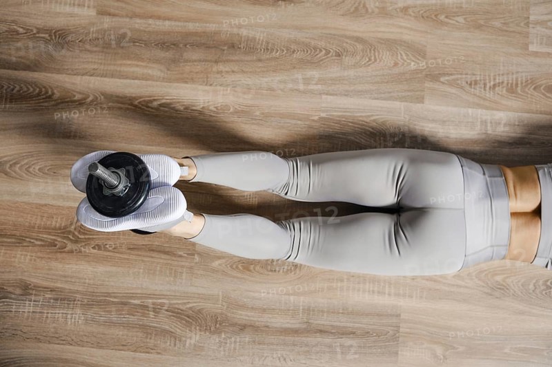 Top view of muscular legs of athlete lifting a dumbbell sandwiched between her feet