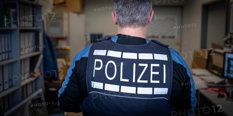 Police officer in office, back view, surrounded by files and computers, symbolic image search, Germany, Europe