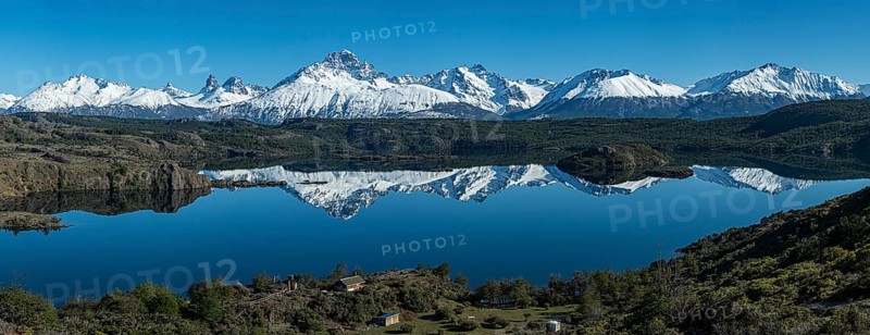 The snow-covered Mt. Cerro Castillo is reflected in a lake, small farm by the lake, Panorama, Patagonia, Chile, South America