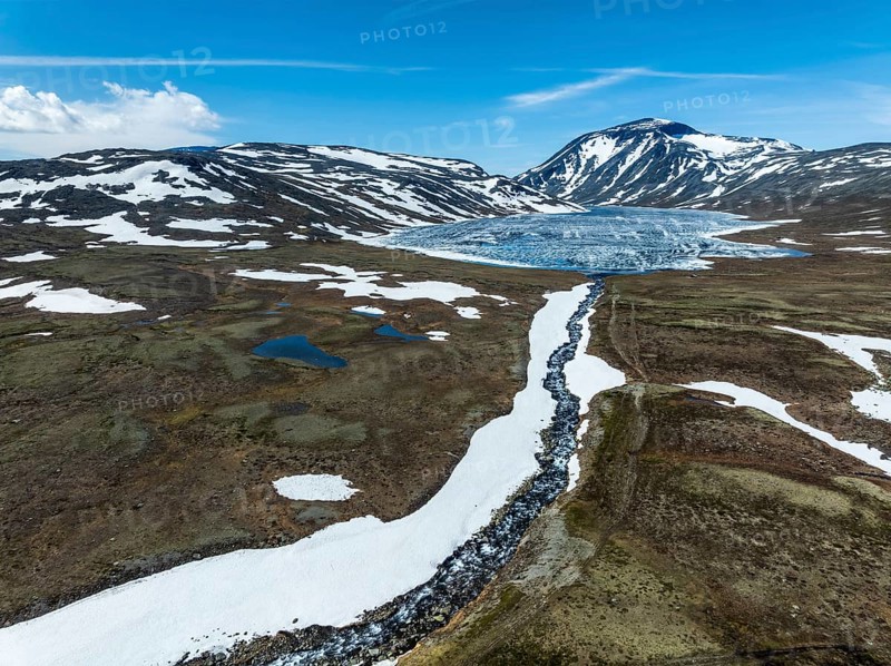 Melting ice on mountain lake Bessvatn, Mt. Besshö, river Bessa, old snow in early spring, aerial view, Jotunheimen National Park, Norway, Europe