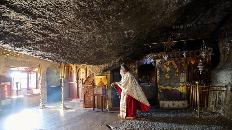 Priest in a sacred space carved into the rock in front of a decorated altar, rock grotto, Monastery of tis Apokalipsis, Patmos, Dodecanese, Greek Islands, Greece, Europe