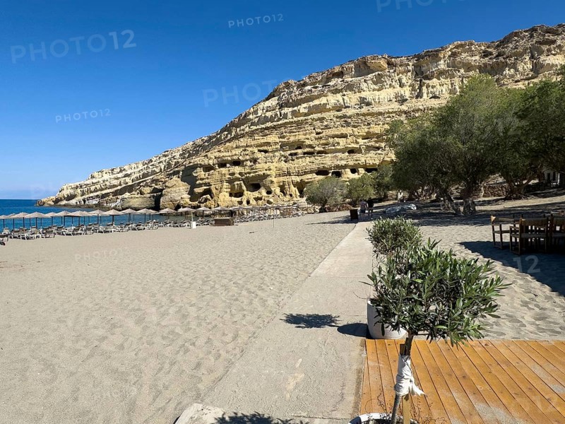 View of Matala beach, in the background sandstone rocks with former Roman necropolis with sandstone caves carved into sandstone Cave tombs Grottoes in rocks on the north side of Matala bay, in the 60s and 70s hippie caves Caves for dropouts and hippies today excursion destination on the south coast of Crete island, left at the edge of the picture Libyan Sea Mediterranean Sea, Matala, Crete, Greece, Europe