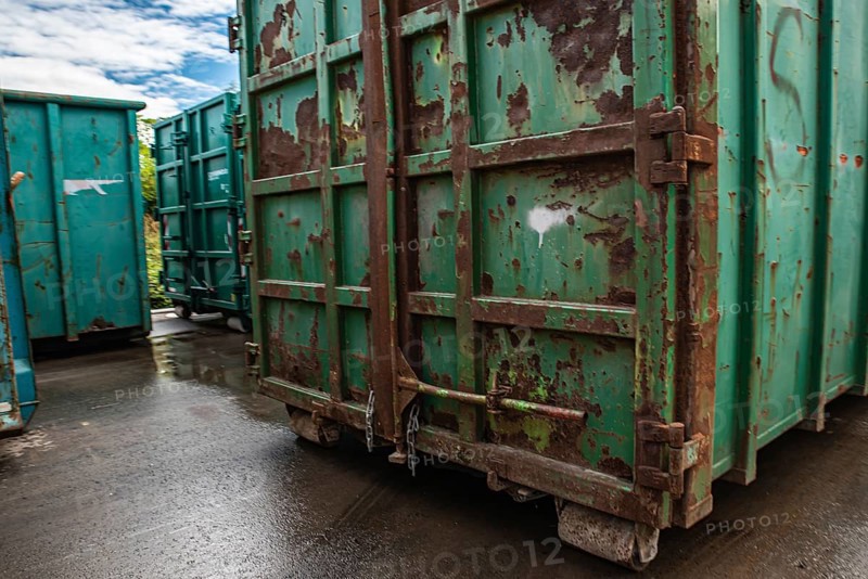 Large green containers with rust stains stand on a rain-soaked industrial site