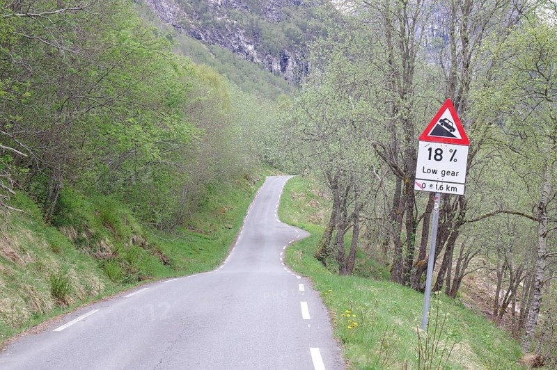 A winding mountain road through a dense forest with a sign indicating an 18 per cent gradient, Stalheimskleiva, Fjordland, Norway, Europe