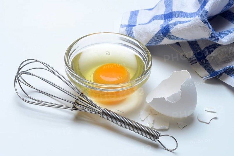 Egg whites and egg yolks in glass bowl and egg shells, whisk