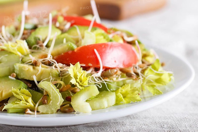 Vegetarian salad of celery, germinated rye, tomatoes and avocado on linen tablecloth, close up, selective focus, side view