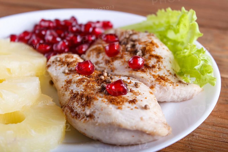 Fried chicken fillets with lettuce, pineapple and pomegranate seeds on brown wooden background, close up