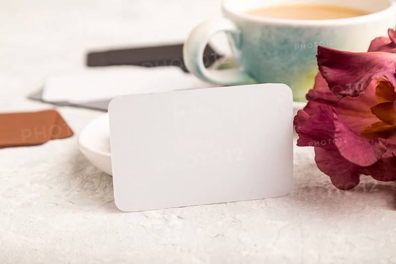 White business card with cup of cioffee, chocolate candies and iris flowers on gray concrete background. side view, copy space, still life. Breakfast, morning, spring concept