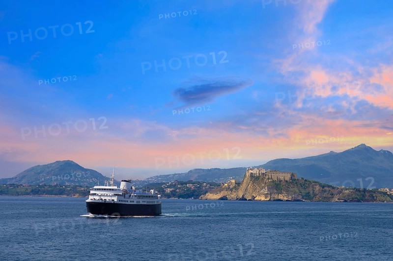 Italy, scenic sunset over Procida Island near Naples with boat approaching it from afar, Europe