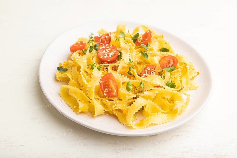 Reginelle semolina pasta with tomato, eggs, sesame and microgreen sprouts on a white wooden background. Side view, close up