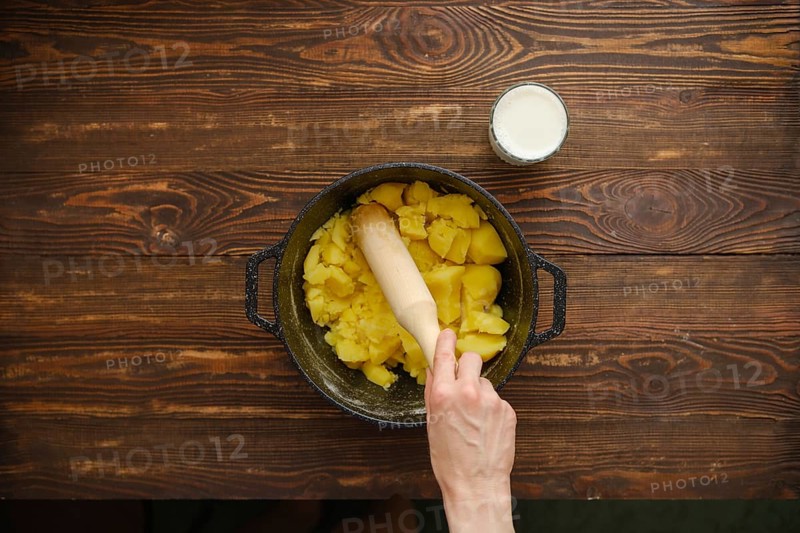 Hand of woman holds wooden potato masher and making mashed potatoes, top view