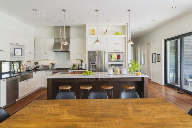 Open-concept dining and kitchen area with antique dining table with black leather and plastic chairs, marble top wooden island with painted black steel and exotic wood bar stools, white cabinets inside a luxurious modern cube style house, Quebec, Canada. This image is property released. CUPR0343