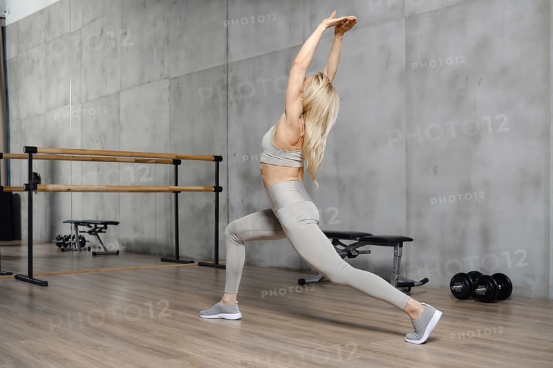 Rear side view of fitness woman bends backward stretching the muscles of her back and arms