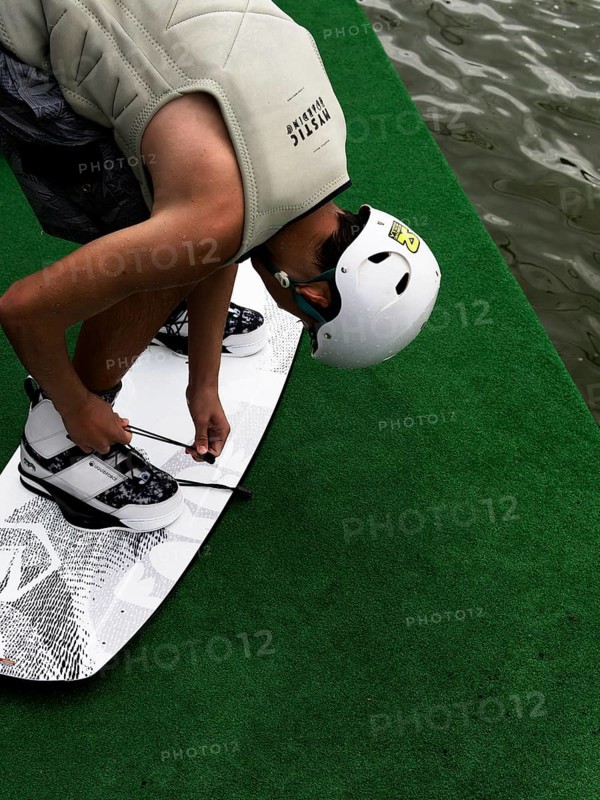 Young man with helmet and wakeboard, tying shoes in front of jump start, water sports