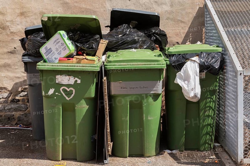 Green and grey plastic recycling and thrash bins filled with cardboard and black garbage bags in a back alley, Old Montreal, Canada, North America