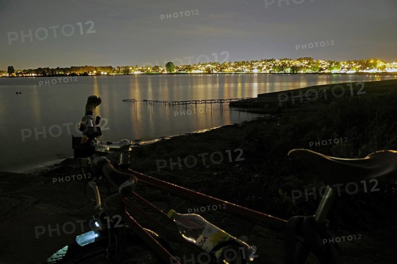 Night view of a lake with illuminated city in the background, bicycle in the foreground, Tönsberg, Oslofjord, Norway, Europe