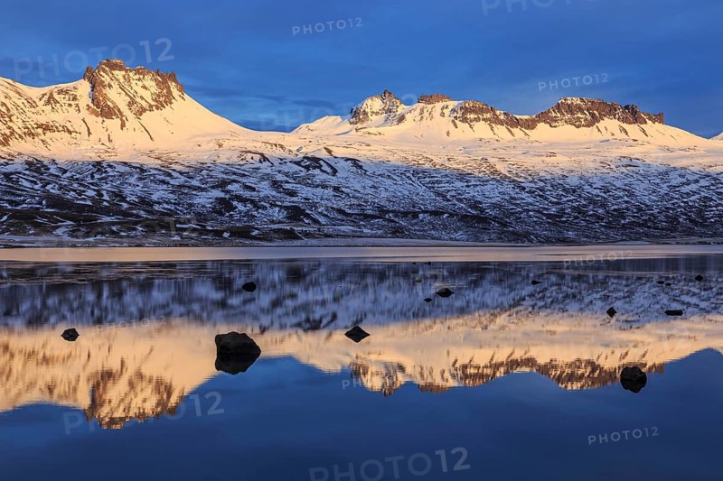 Snow-covered mountains reflected in a fjord in the evening light, Berufjördur, East Fjords, Iceland, Europe