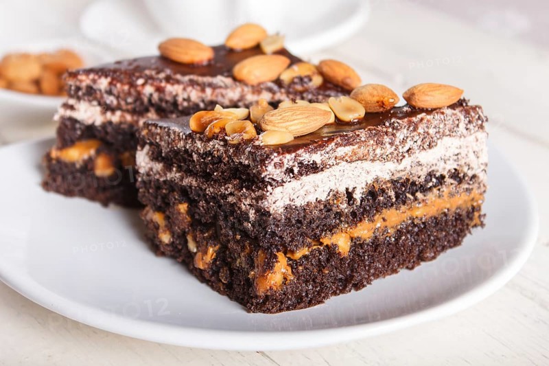 Chocolate cake with caramel, peanuts and almonds on a white wooden background. cup of coffee, top view, close up