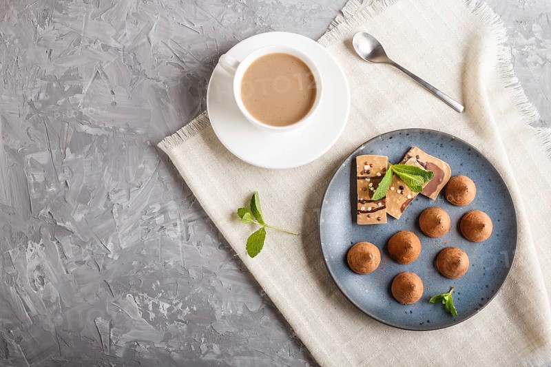 Chocolate truffle on blue ceramic plate and a cup of coffee on gray concrete background. top view, copy space