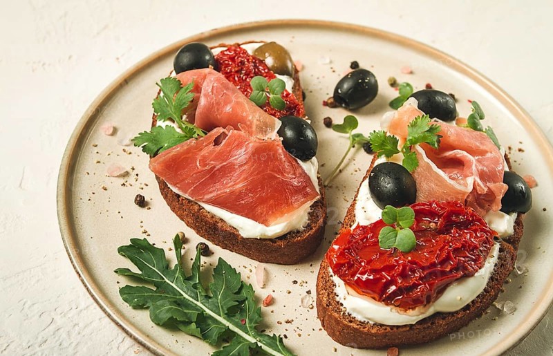 Sandwiches with cheese and prosciutto, dried tomatoes and olives, breakfast on a plate