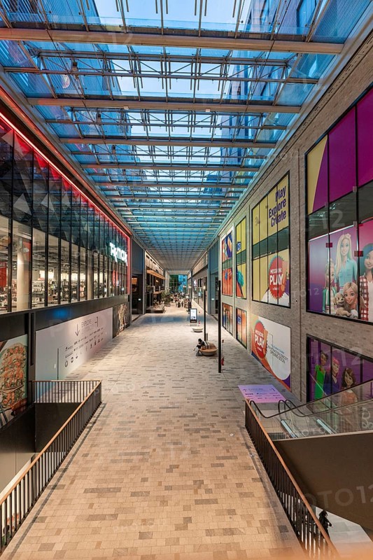 Modern shopping centre with glass roof, brightly lit and lined with shops. Colourful advertising banners on the walls, Berlin, Germany, Europe