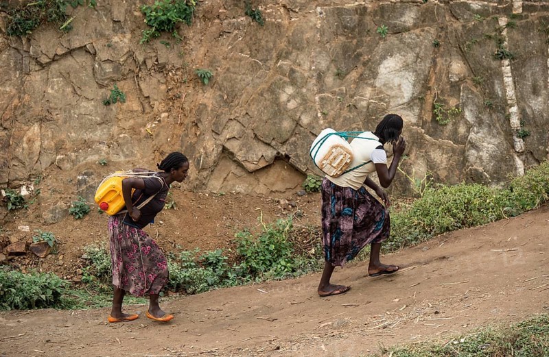 Two woman carry heavy water canisters on their backs from the water point to the village, near the village of Konso, southern Ethiopia