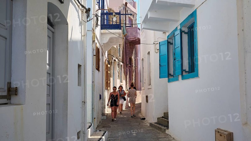Narrow alley with white walls and colourful shutters, strollers in summer, Mandraki, Nisyros, Dodecanese, Greek Islands, Greece, Europe