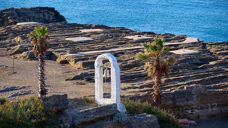 View of a rocky coastline with palm trees, a white bell frame and blue sky in the background, rock church of Agios Nikolaos, Oasis Beach, Kallithea, Rhodes, Dodecanese, Greek Islands, Greece, Europe