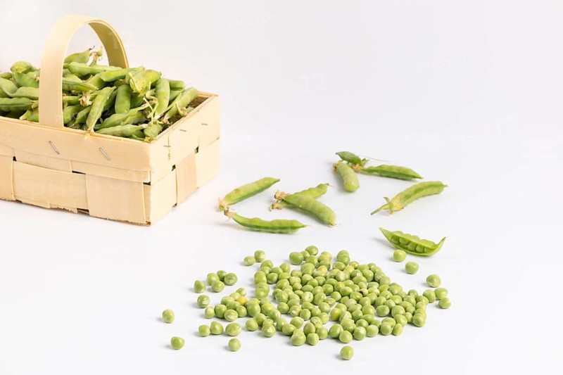 Pea pods and peas (Pisum sativum) in front of and in wooden baskets on a white background