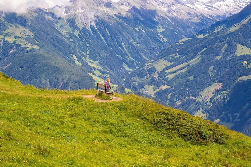 A woman sits on a bench and looks at the vast valleys and mountains, Penken, Zillertal, Austria, Europe