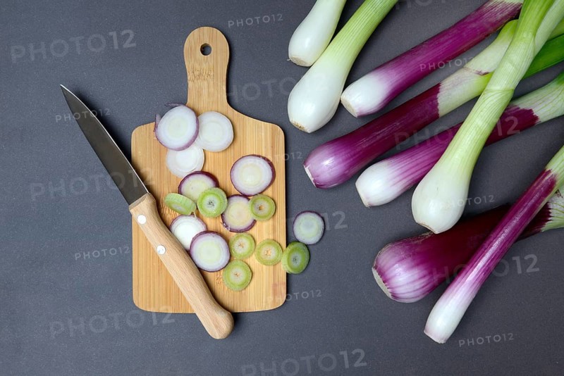 Spring onions and onion rings with a knife on a wooden board, spring onion