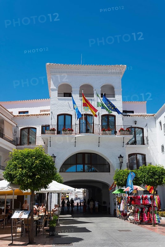 City gate of a whitewashed building on a square with flags and shops under a clear blue sky, town hall, Nerja, Málaga province, Malaga, Andalusia, Spain, Europe