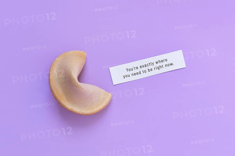 Fortune cookie with motivational text on paper saying 'You're exactly where you need to be right now' on violet background