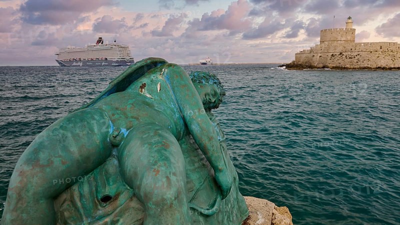 A damaged sculpture looks out over the sea and a fortress during a dramatic sunset, sky exchanged, sculpture Sleeping Eros, cruise ship, Fort of Saint Nikolaos, harbour area, Rhodes Town, Rhodes, Dodecanese, Greek Islands, Greece, Europe