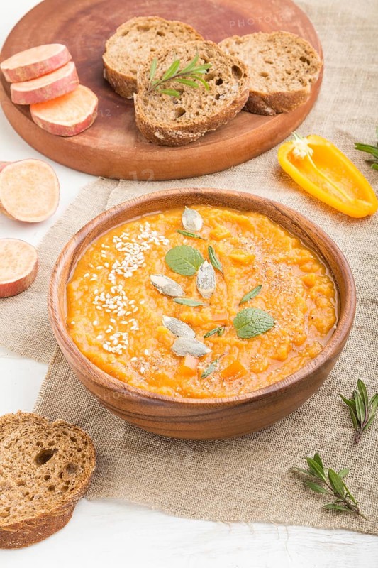 Sweet potato or batata cream soup with sesame seeds in a wooden bowl on a white wooden background with linen textile. side view, close up
