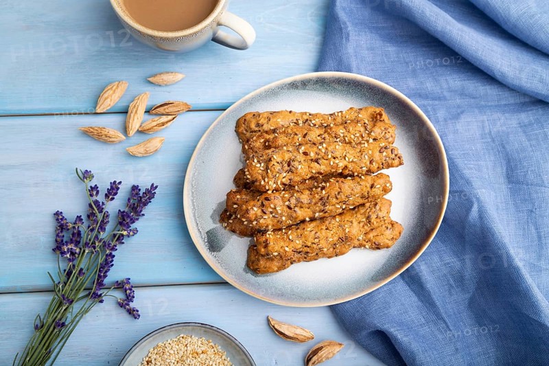 Crumble cookies with seasme and almonds on ceramic plate with cup of coffee and blue linen textile on blue wooden background. top view, flat lay, close up